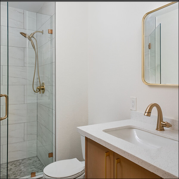 After: Refined bathroom with a glass shower, warm wood vanity, and coordinated gold accents